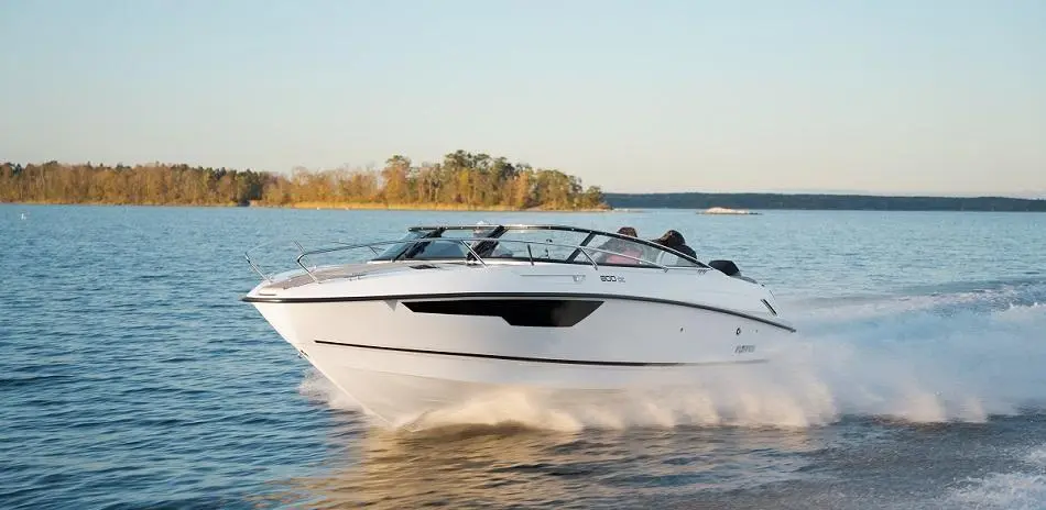 White powerboat speeding across a calm lake, surrounded by trees and blue sky, creating splashes of water.